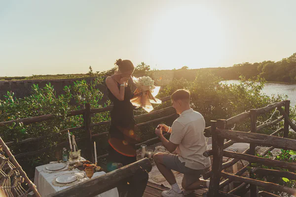 Propuesta al atardecer en una terraza rústica con vista a los manglares de Puerto Morelos; la mesa, vestida con sábanas blancas impecables, vajilla elegante y altas velas, se funde en un ambiente bohemio y romántico gracias a la luz dorada de la hora mágica.