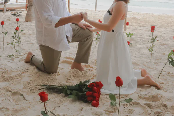 Propuesta en la famosa Playa Ruinas de Tulum sobre arena blanca inmaculada, donde rosas rojas individuales trazan un camino romántico natural bajo las antiguas ruinas mayas; la pareja descalza encarna el lujo desenfadado de una ceremonia costera al amanecer.