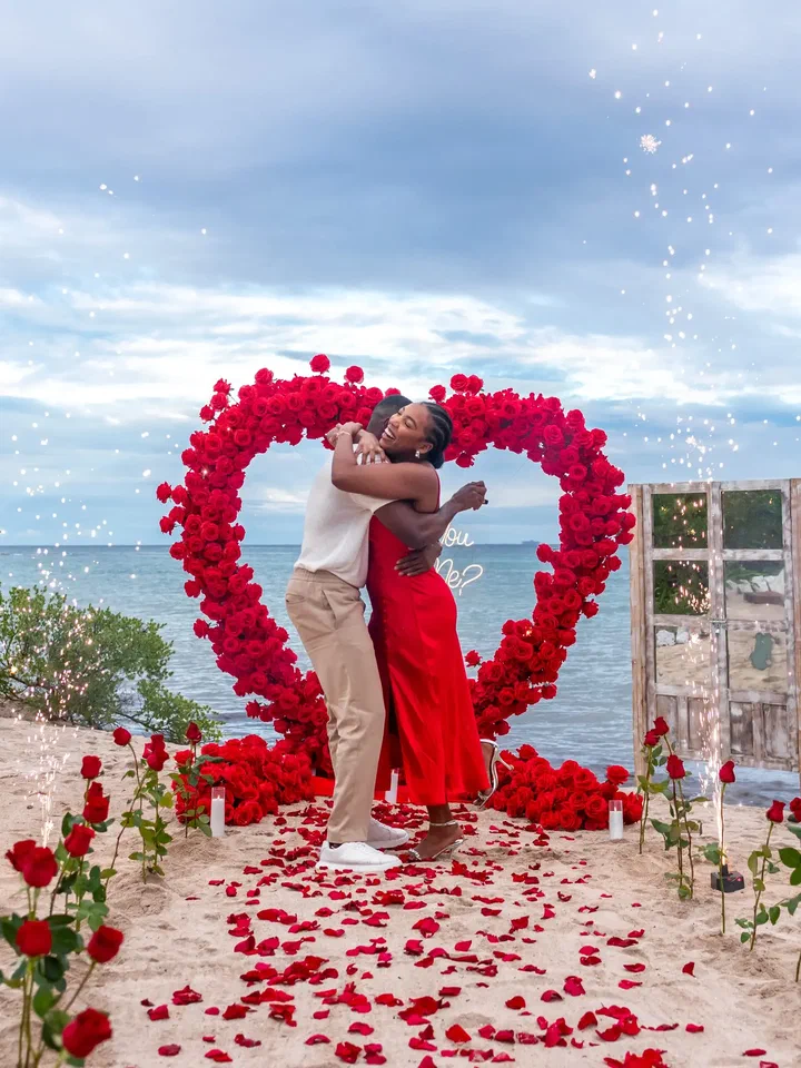 Couple embracing in front of a red rose heart on the beach as sparklers go off