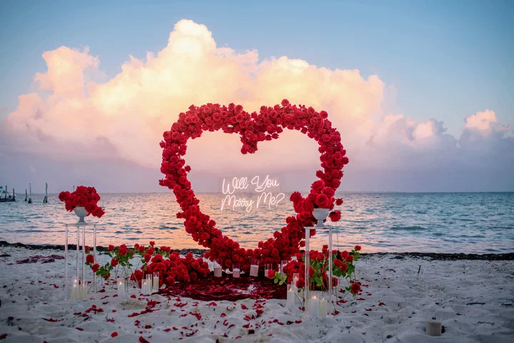 Corazón de rosas rojas con letrero “Will You Marry Me?” en la playa al atardecer