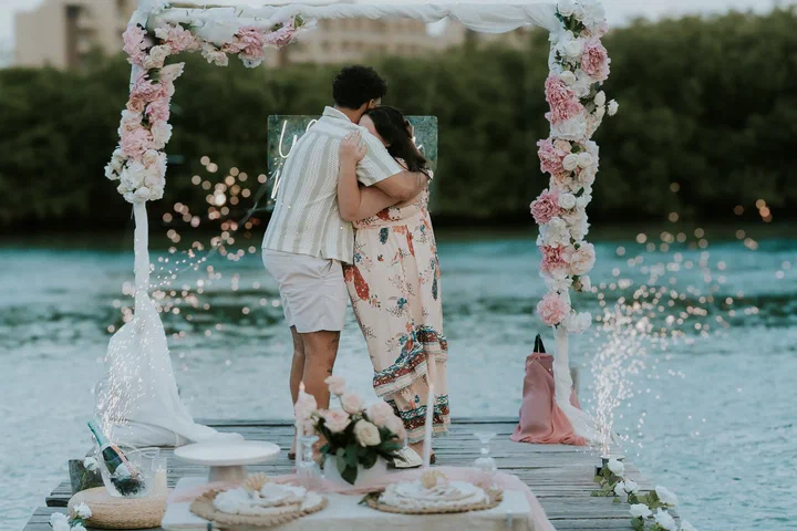 Pareja abrazada bajo un arco de flores en un muelle de la laguna con chisperos